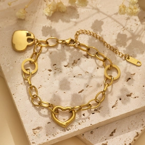 Polished gold heart charm bracelet with adjustable chain on a travertine surface