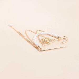 Dettaglio spilla da balia vintage dorata con perle multistrato e catene metalliche pendenti