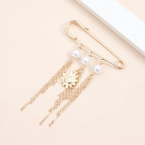 Vintage gold brooch pin with white pearls, tassels and sun face pendant on beige background