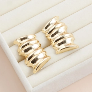 Détail de boucles d'oreilles dorées avec design ondulé sur plateau en velours blanc