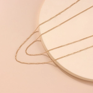 Elegante goldfarbene mehrlagige Körperkette mit langen Quasten auf rosa Hintergrund