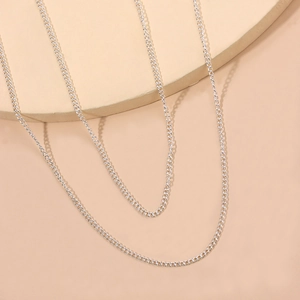 Elegante doppellagige silberne Metall-Taillenkette mit langen Quasten auf beigem Podest