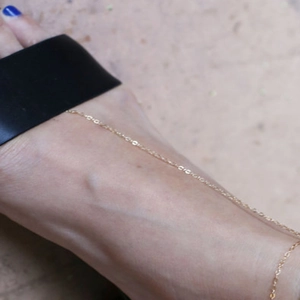 Cavigliera minimalista dorata da donna indossata con sandali neri e sfondo in pietra