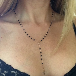 Detail of Y-shaped necklace with black beads and gold cross pendant on a female model