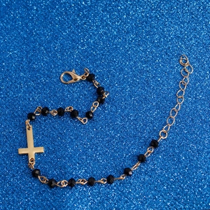 Detail view of gold cross bracelet with black faceted beads and lobster clasp closure