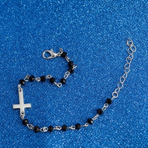 Detailed view of beaded bracelet with black faceted beads and silver cross pendant
