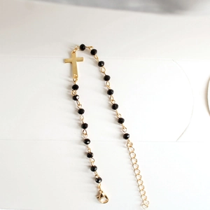 Detail view of a gold cross pendant on a black beaded bracelet with adjustable lobster clasp