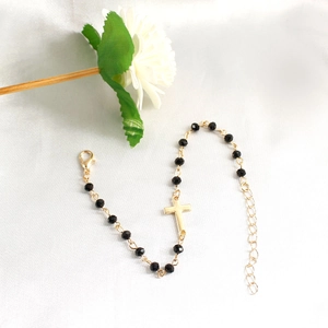 Close-up of black beaded bracelet with gold cross charm and adjustable lobster clasp