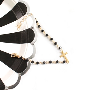 Close-up of gold-tone cross bracelet with black faceted beads and lobster clasp closure
