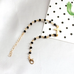 Detail of beaded bracelet showing gold cross pendant and black faceted beads with clasp
