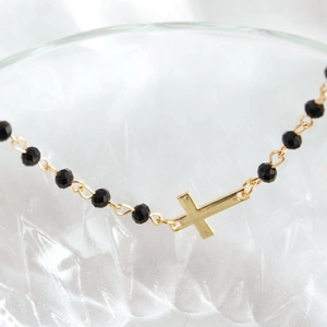 Detail of beaded bracelet featuring gold cross pendant and black multifaceted beads