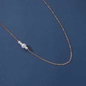 Détail d'une chaîne de taille dorée ornée de quatre perles blanches sur fond bleu marine