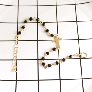 Detail of beaded cross bracelet with black faceted beads and gold plated extender chain
