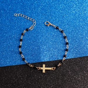 Detail of beaded bracelet featuring gold cross charm and black faceted beads with clasp