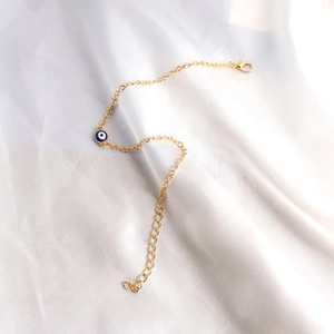 Detailed view of a gold evil eye bracelet on white satin with an adjustable lobster clasp