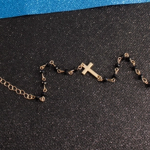 Close-up of golden cross pendant with black faceted beads and adjustable chain link