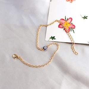 Close-up of golden chain bracelet with blue evil eye bead on white satin background