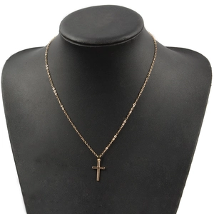 Primer plano de un collar con colgante de cruz dorada minimalista en un busto negro