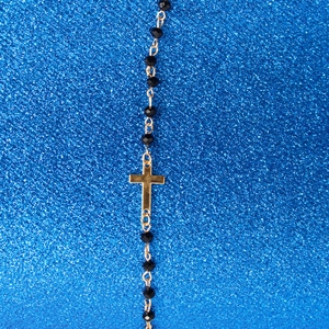 Macro shot of gold cross pendant with black beads on a vibrant blue textured background