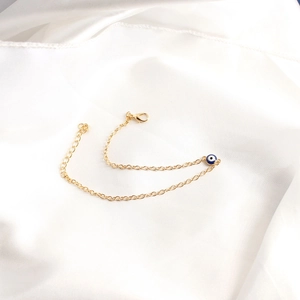 Close-up of golden link bracelet featuring a blue evil eye pendant on white silk background