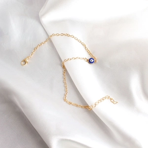 Detailed shot of golden link bracelet with blue evil eye charm on white satin