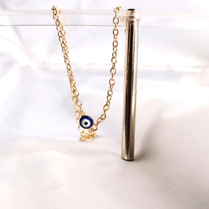 Detailed close-up of a delicate golden chain bracelet featuring a blue Evil Eye pendant charm