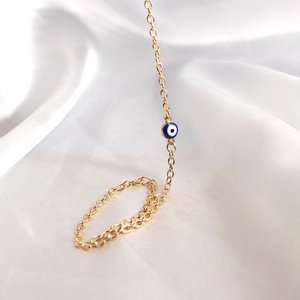 Close-up of golden chain bracelet with blue evil eye charm on white silk background