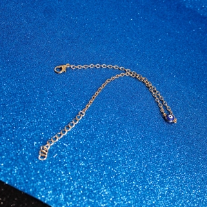 Close-up of golden Evil Eye bracelet with blue bead charm and lobster clasp detail