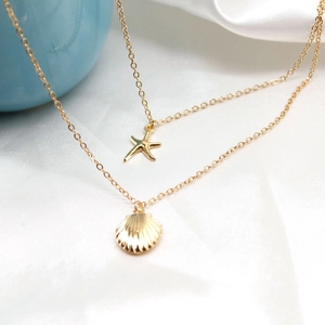 Detail of layered gold necklace featuring starfish and seashell charms on silk