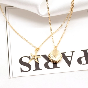 Detail of layered gold necklaces with starfish and seashell pendants on white satin