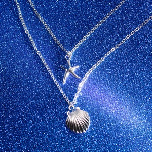 Close-up of double-layer silver starfish and shell pendant necklace on a blue starry backdrop
