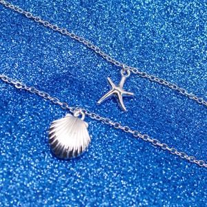 Detail of silver layered necklace showing starfish and seashell charms on blue glitter
