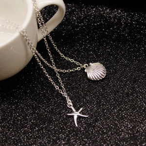 Detailed macro view of silver shell and starfish charms on a layered necklace chain