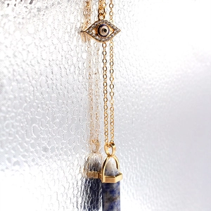 Detailed macro view of gold evil eye pendant and blue stone hexagonal column necklace