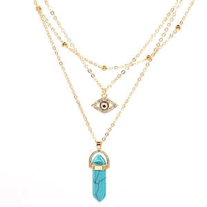 Detail of multi-layered gold necklace with hexagonal turquoise pendant and evil eye charm