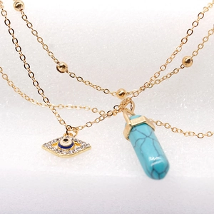Macro shot of gold layered necklace with evil eye charm and turquoise hexagonal prism
