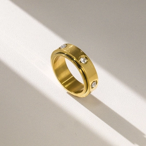 Detail of golden stainless steel anxiety ring featuring rotating band and zircon stones