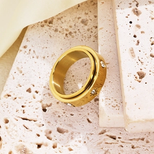 Close-up of golden rotatable stainless steel ring with zircon stones on stone surface