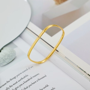 Bracciale rigido dorato lucido a forma rettangolare con diamante su sfondo minimalista