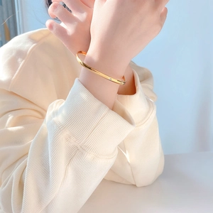 Dettaglio ravvicinato di un bracciale rigido dorato minimalista con piccola gemma incastonata