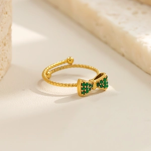 Detail eines gedrehten Goldrings mit grüner Strass-Schleife auf Marmorsockel