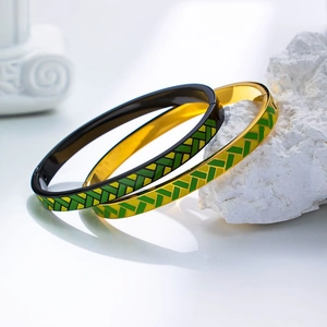 Dettaglio di bracciali minimalisti oro e nero con motivi geometrici verdi in diagonale