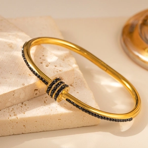 Detail eines vergoldeten Edelstahl-Armreifs mit schwarzen Steinen und Anhänger-Ringen