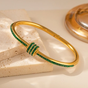 Detail eines goldenen Bambusarmbands mit grünem Kristallbesatz auf Steinhintergrund