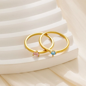 Detalle de anillos minimalistas de titanio dorado con piedras rosa y azul en seda