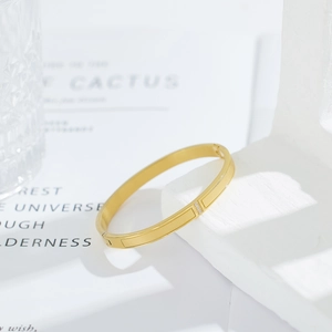 Close-up of gold stainless steel bangle with three clear zircons on white stone base