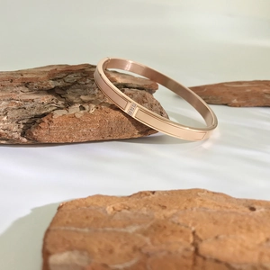 Polished 18K rose gold stainless steel bangle with three zircon stones on wood
