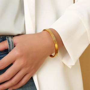 Close-up of golden stainless steel bangle featuring engraved meander geometric patterns