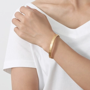 Titanium steel bangle with Greek meander pattern worn on model wrist in gold finish