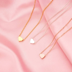 Close-up of heart necklaces in gold, silver and rose gold on pink silk fabric
